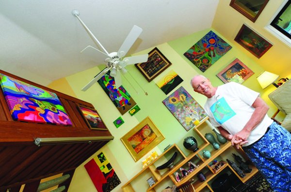 Artist Frank Oliva working at his easel in a bright, sunlit Kailua studio, surrounded by vibrant Aboriginal-inspired dot paintings in various stages of completion, paint supplies scattered on tables, creating colorful artwork in an inspiring creative space filled with natural light